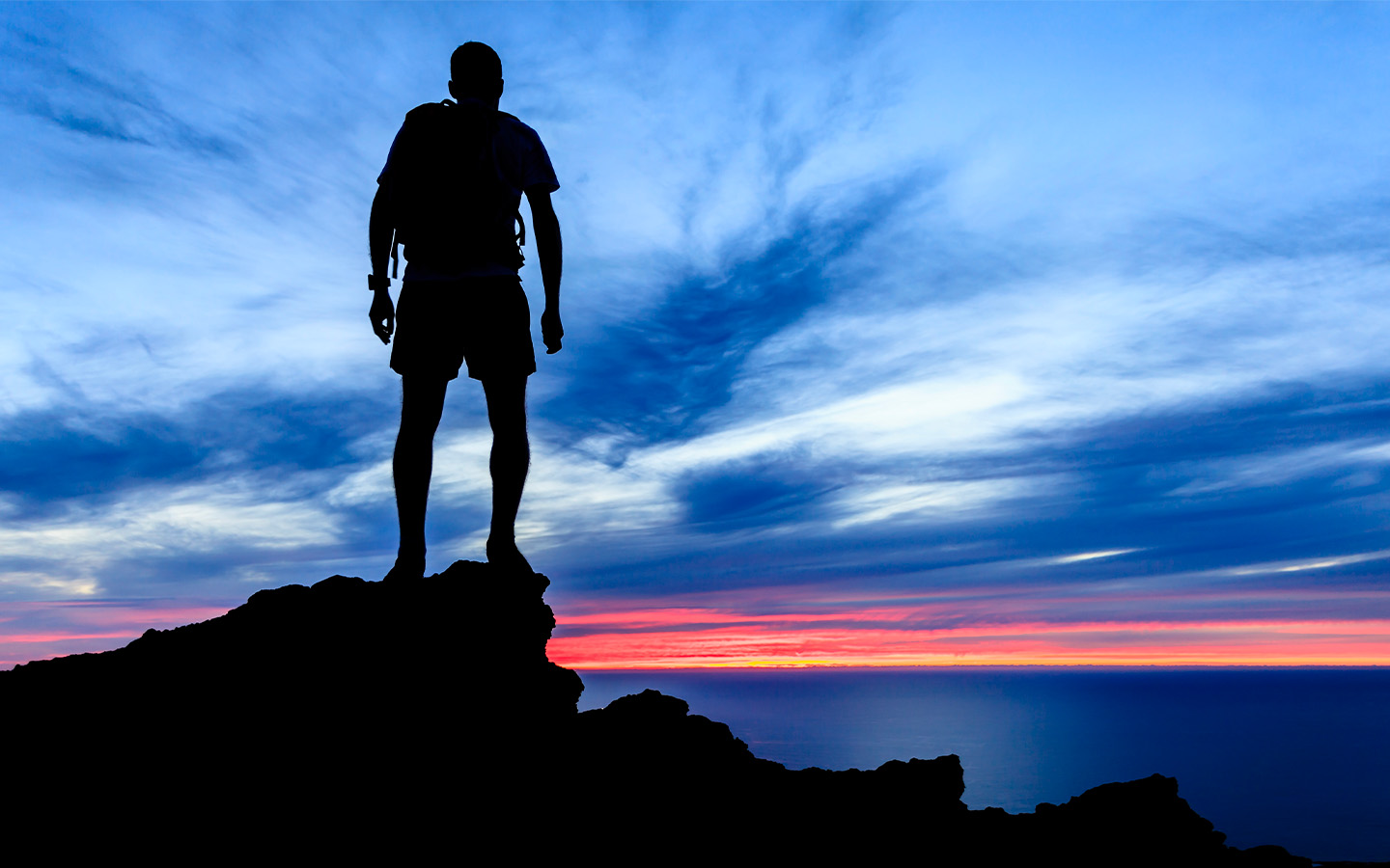 Uomo che ha raggiunto il suo obiettivo e guarda il tramonto da una scogliera